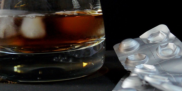 A snifter glass of liquor with ice sits on a black table with a mostly used package of pills arranged beside it. It is unclear what the medication is.