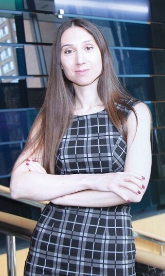 Amanda stands leaning on a staircase banister smiling at the camera. Her arms are crossed over each other.