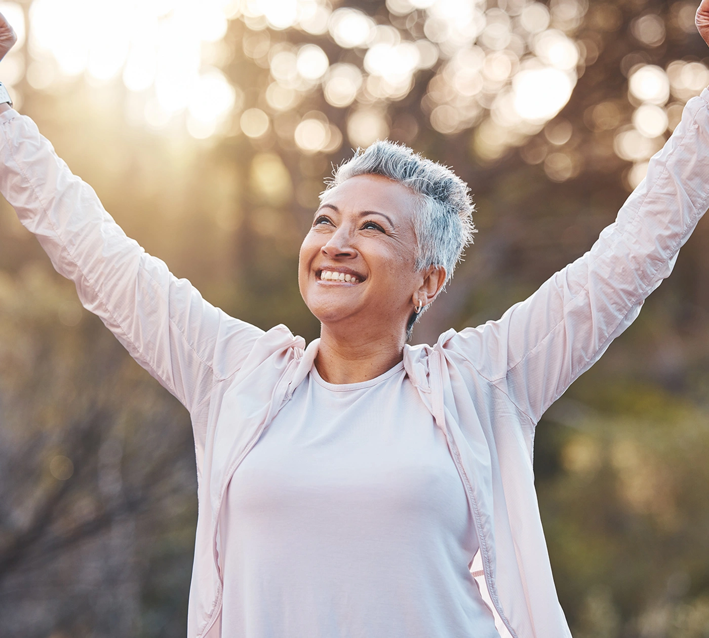 Elderly woman smiling with her arms raised outdoors at sunset